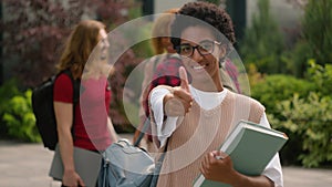 Students talking near university campus outdoors African American happy satisfied student girl woman showing thumb up