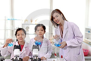 Students and teacher in lab coat have fun together while learn science experiment in laboratory. Young pretty Asian scientist and