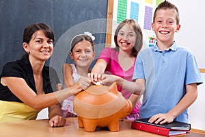 Students and teacher putting coin into piggy bank