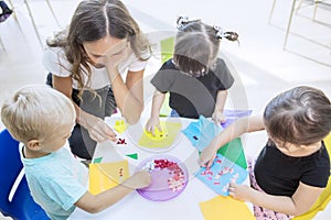 Students and their teacher gluing trinkets on a paper