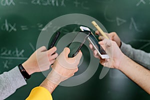 Students using mobile phones in classroom with a chalkboard in the background.