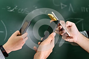 Students using mobile phones in classroom with a chalkboard in the background.