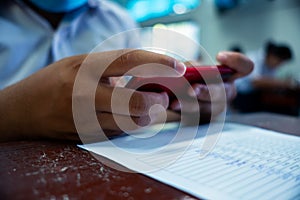 Students using smartphone and doing exam answer sheets exercises in classroom of school