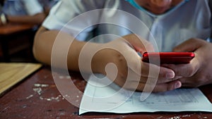 Students using smartphone and doing exam answer sheets exercises in classroom of school