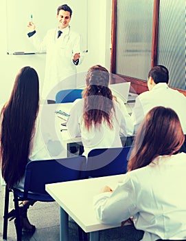 Students in white coats listen to lecture in audience