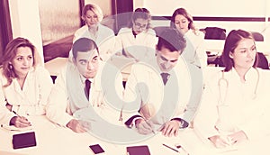 Students in white coats listen to lecture