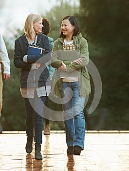 Students, women and friends on campus for college, conversation while walking to class and smile. University