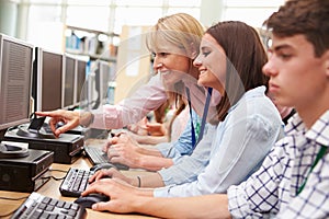 Students Working At Computers In Library With Teacher