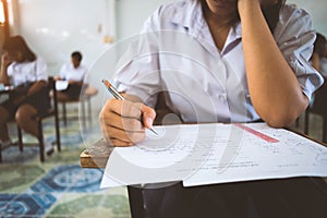 Students writing pen in hand doing exams answer sheets exercises in classroom with stress