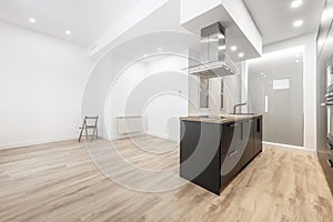 Studio apartment with an open kitchen with an island with black furniture, a wooden worktop with a sink and a ceramic hob under photo