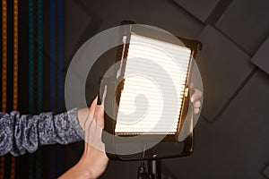 Studio assistant fix professional video light on adjustable light stand. Led lamp on tripod in photo studio. Photo and video lamp