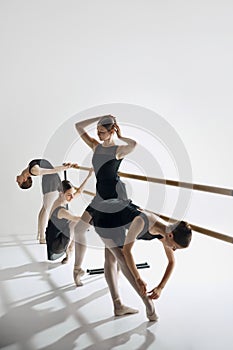 Studio ballet practice. Elegant teen girls practicing at dance class, standing at barre and training against grey studio
