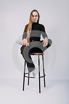 Studio candid unaltered portrait of young blonde woman with long hair sitting on chair. Portrait of Fashionable stylish