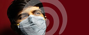 Studio close-up portrait of male face wearing medical flu mask, on background of dark red color with copy space.