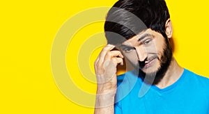 Studio close-up portrait of young guy feeling doubt emotions, wearing blue shirt, holding hand on head, background of yellow color