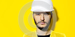 Studio close-up portrait of young serious man architect, builder engineer, wearing white construction safety helmet and yellow jac