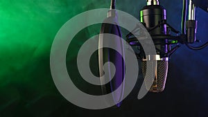 Studio condenser microphone with pop-filter and anti-vibration mount with backlight, color purple and green smoke. Side view with