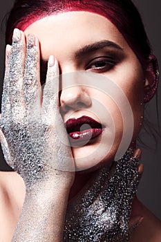 Studio fashion portrait of attractive woman with creative make-up and glitter and spangle on hands