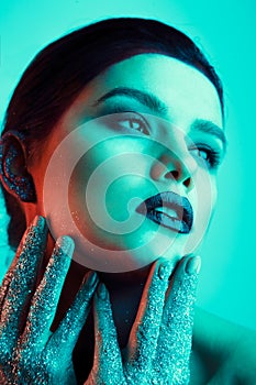 Studio fashion portrait of attractive woman with creative make-up and glitter and spangle on hands. Mint light.