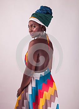 Studio fashion portrait of young African woman in summer dress and ethnic head wrap, white background