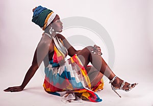 Studio fashion portrait of young African woman in summer dress and ethnic head wrap, white background