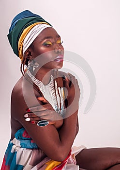 Studio fashion portrait of young African woman in summer dress and ethnic head wrap, white background