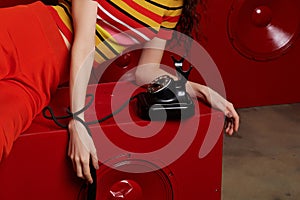 Studio fashion shooting.The girl in a bright outfit, top and pants flared in red and orange tones. Hands with phone