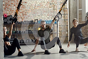 Studio Fitness. Portrait of man and women doing fitness TRX training exercises at industrial gym. Push-up, group workout