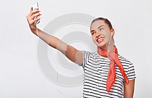 Studio horizontal portrait of beautiful European young woman taking self portrait over white wall, wearing striped t-shirt and red