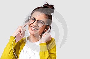 Studio horizontal portrait of pretty happy young woman smiling broadly, using cellphone to listening the music