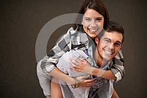 Studio, hug and portrait of happy couple, piggyback ride and having playful fun together on brown background. Wellness