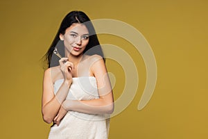 Studio image of beautiful young woman, girl with white towel around her body isolated on yellow studio background.