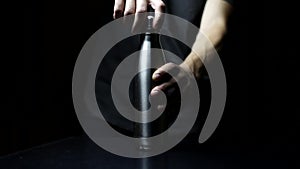 Studio image, close-up of male hand puts on lid for reusable, steel thermo water bottle on black background.