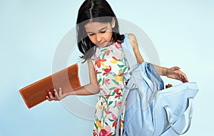 Studio image of a cute little girl wearing summer dress preparing her backpack in the morning for the school summer camp posing