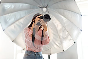 Studio magic. Young photographer woman capturing moments with professional camera in front of reflective umbrella