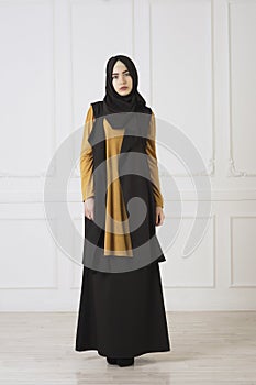 Studio photo in full growth beautiful girl looks in the eastern Muslim dress and black scarf on head