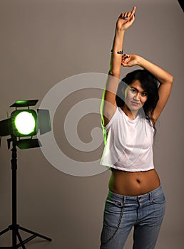 Studio photo of a girl with a yellow spotlight. Girl posing at camera with raised hand and protruding finger. A young girl in