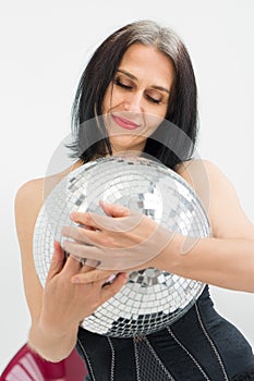 Studio photo of middle aged woman starting getting grey-haired wearing black clothes with silver disco ball in hands on