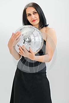 Studio photo of middle aged woman starting getting grey-haired wearing black clothes with silver disco ball in hands on