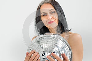 Studio photo of middle aged woman starting getting grey-haired wearing black clothes with silver disco ball in hands on