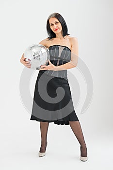Studio photo of middle aged woman starting getting grey-haired wearing black clothes with silver disco ball in hands on