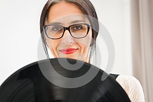 Studio photo of middle aged woman starting getting grey-haired wearing black and white clothes with vinyl record in