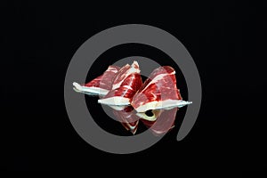 studio photo of a series of slices of 100% Iberian acorn-fed ham folded on black background with reflection