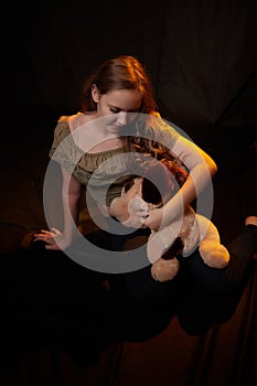Studio photo shot of young teenager girl with her soft dog toy in hands. Model posing on black background