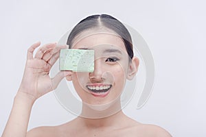 A studio picture of an Asian woman beaming for the camera with a bar of body soap in her hand.