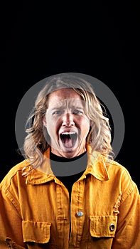 Studio Portrait Of Angry Woman Shouting At Camera Against Black Background