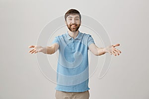 Studio portrait of attractive young male speaker stretching arms towards camera as if talking with audience, expressing