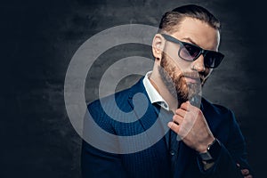 Studio portrait of bearded male dressed in a blue jacket and sunglasses.