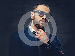 Studio portrait of bearded male dressed in a blue jacket and sunglasses.