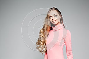 Studio portrait of a beautiful business woman blond with blue eyes with long hair, wears an elegant pink dress and holds